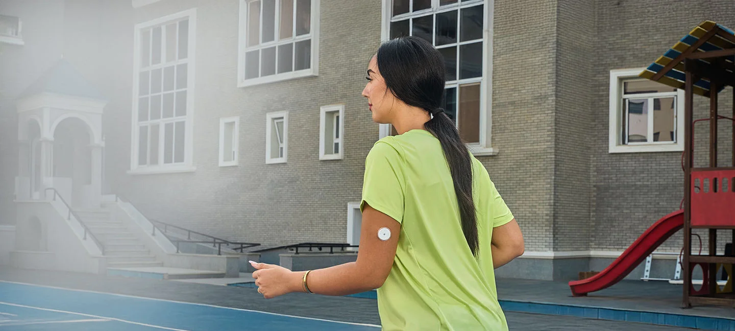 A woman wearing a Freestyle Libre sensor balancing on an exercise ball while smiling broadly.