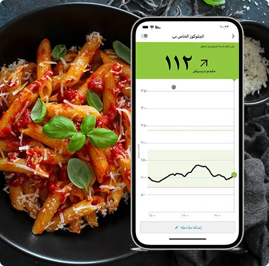  A healthy plate of pasta and marinara sauce. Above the plate is a phone showing a glucose spike on the FreeStyle Libre app.