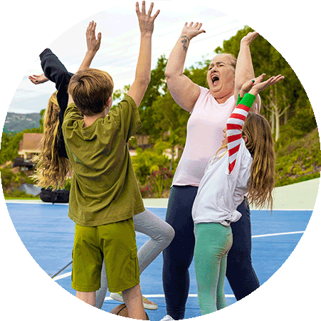 Group of people raising their arms while standing around a basketball on an outdoor court.