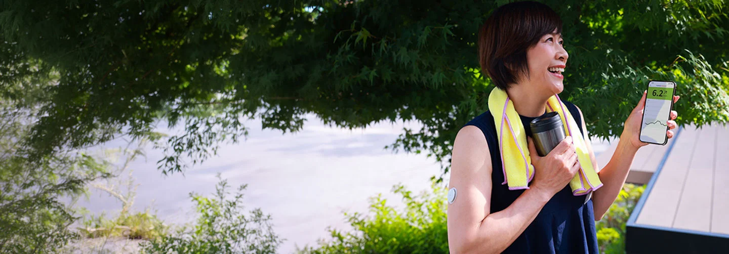 Woman using a FreeStyle Libre glucose monitoring system outdoors while viewing glucose readings on a smartphone.
