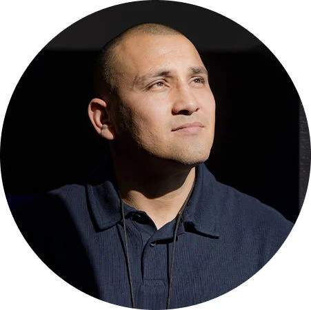 Portrait of a person in a dark shirt looking upward in directional light against a dark background.
