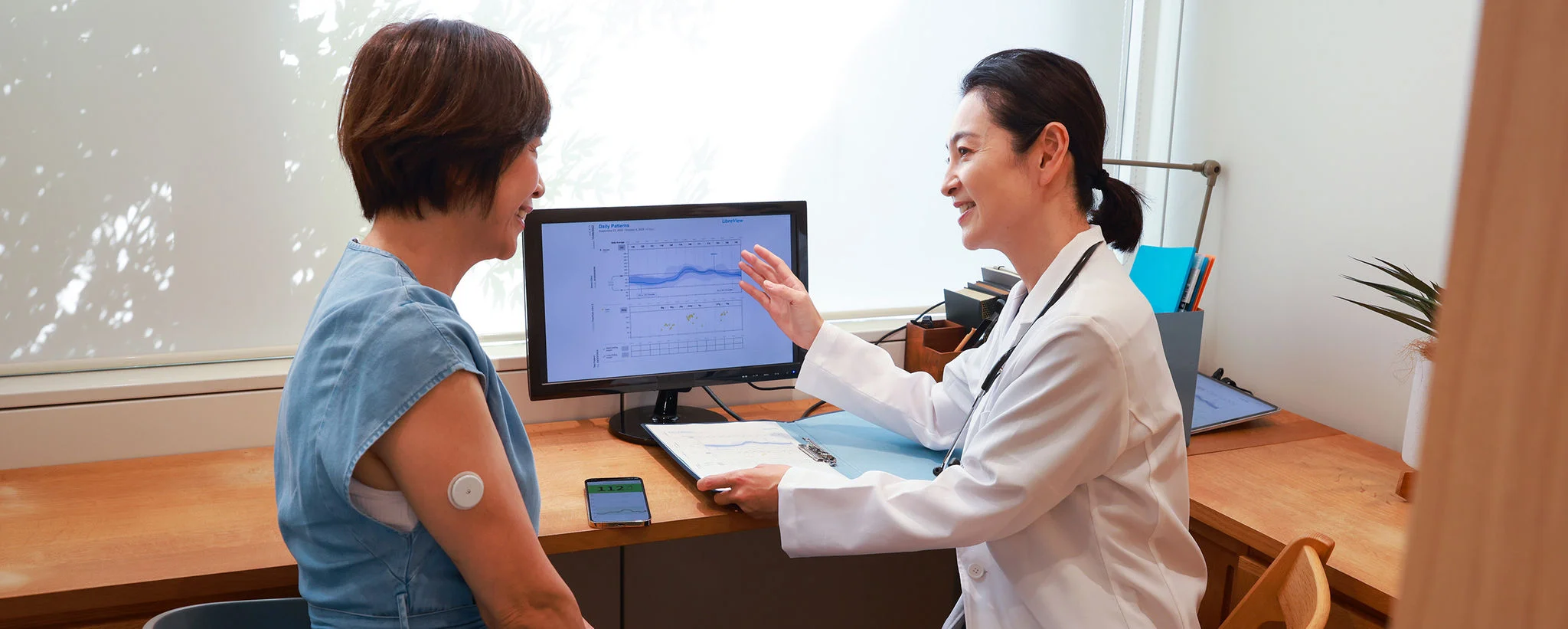 Healthcare professional reviewing glucose data on a computer with a FreeStyle Libre user wearing a sensor during a consultation.