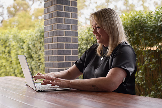 Frau sitzt am Tisch und arbeitet am Laptop.