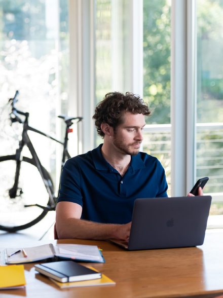 Ein Mann sitzt an einem Schreibtisch mit einem Laptop und einem Smartphone.