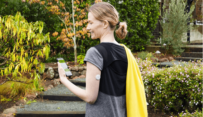 Eine Frau ist draußen unterwegs. Sie hält ein Smartphone in der Hand.