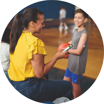 Une mère consultant l'application LibreLinkUp pendant que son fils, qui porte un capteur FreeStyle Libre, tient un ballon de basket dans une salle de sport