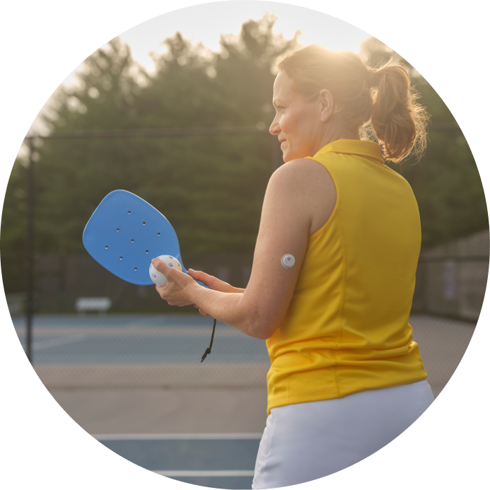 Une femme portant un capteur FreeStyle Libre 3 Plus sur le bras joue au pickleball en extérieur