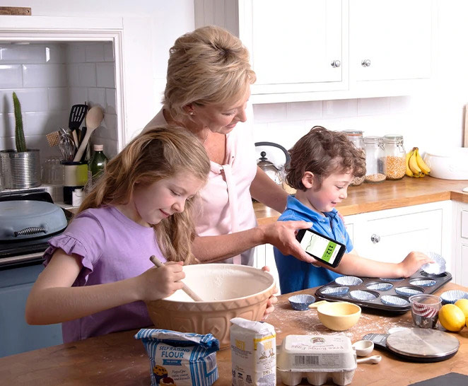 Crianças cozinhando e avó escaneando o Sensor FreeStyle Libre de uma delas com o celular
