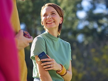 Mulher jovem branca sorrindo enquanto aponta o celular para o sensor de glicose