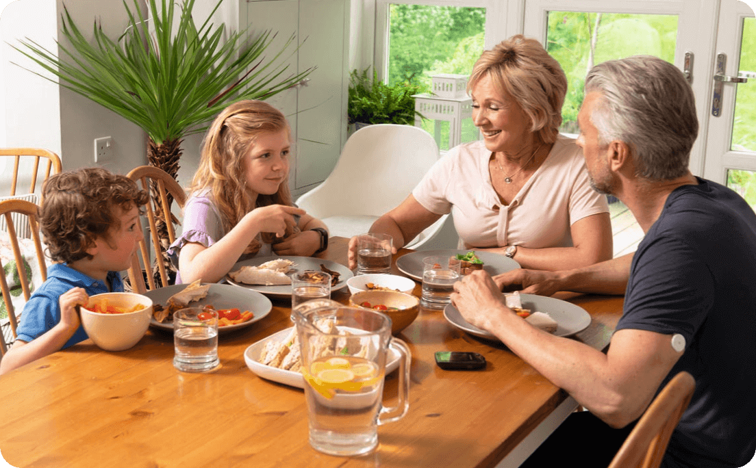 Famiglia composta da due bambini e due adulti seduta a tavola mentre mangia insieme.