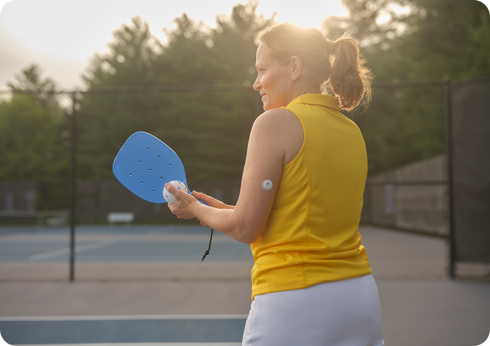 Femme souriante jouant au pickleball et portant un capteur FreeStyle Libre sur le bras