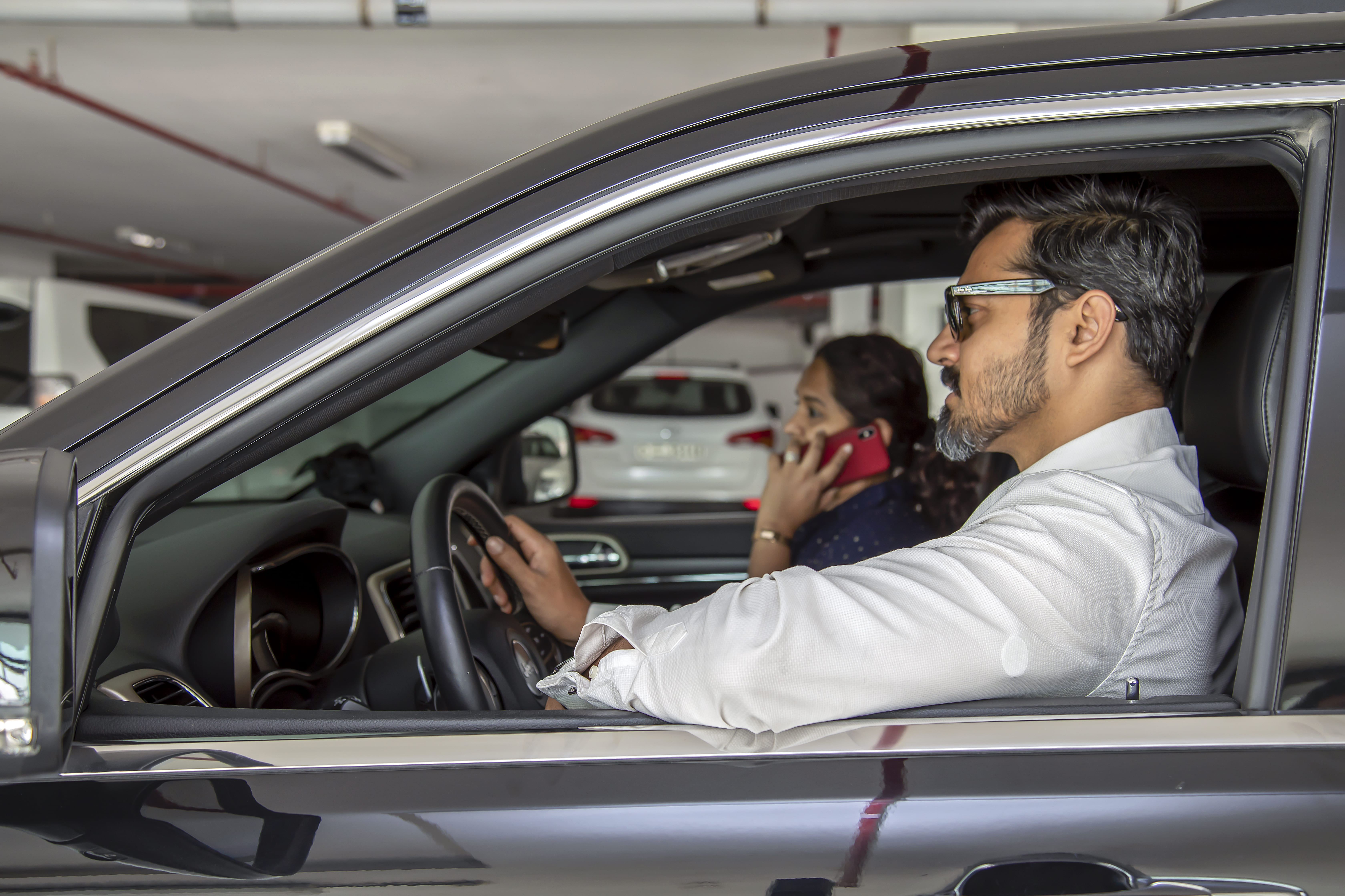 Een man in de auto met een zichtbare sensor op zijn bovenarm onder zijn hemd, en een vrouw naast hem die aan het bellen is op haar gsm.