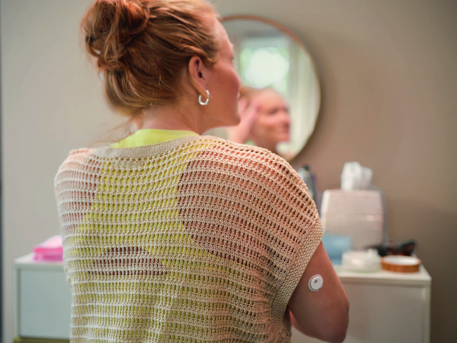 Een vrouw die zich klaarmaakt voor de spiegel, met een sensor op haar bovenarm.