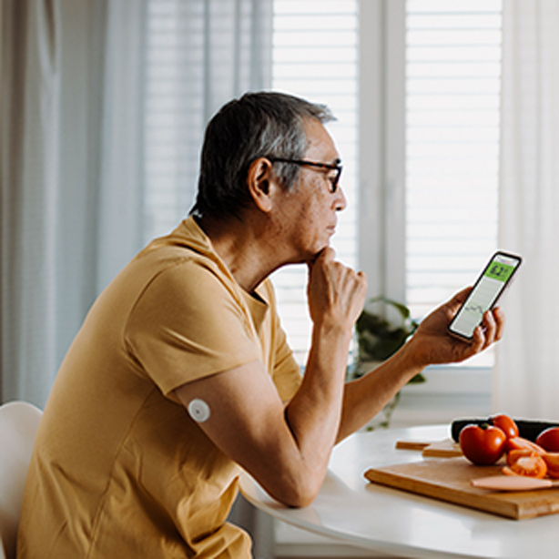 Un homme dans la cuisine avec un capteur sur le haut du bras consultant son gsm.