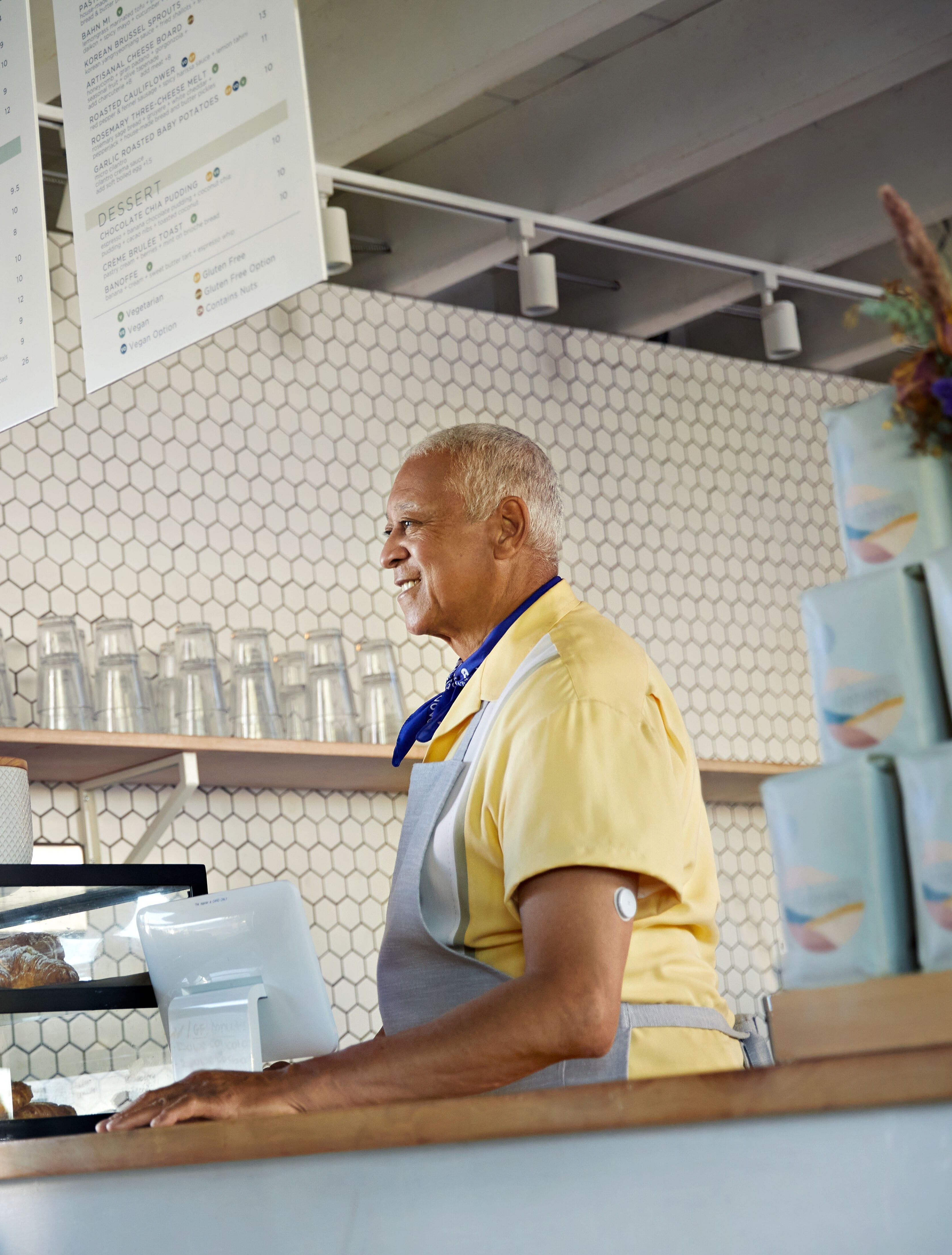 Un barista avec un capteur sur le haut du bras, souriant derrière le comptoir.
