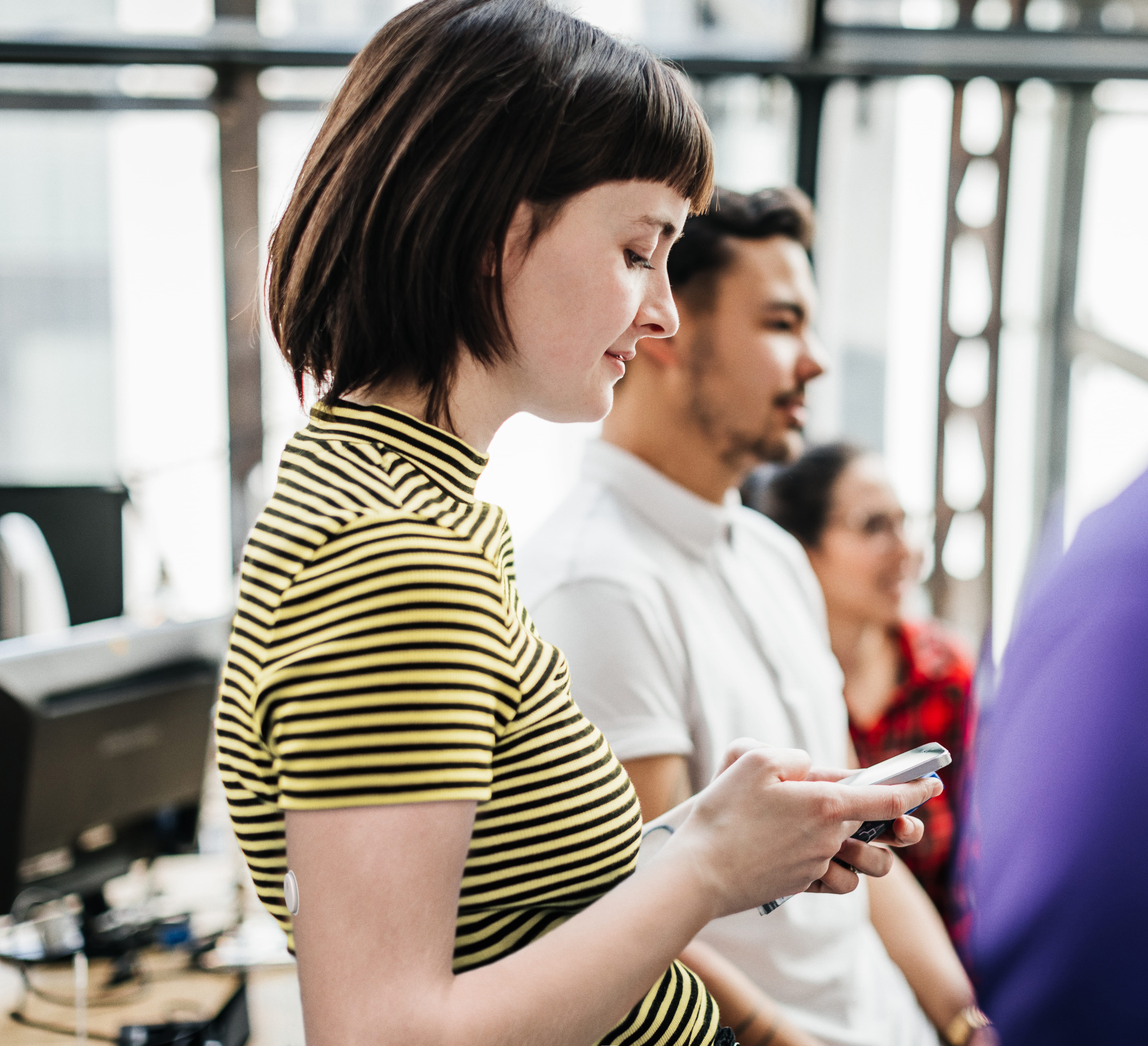 Een vrouw met een sensor op haar bovenarm die naar beneden kijkt en op haar gsm kijkt.
