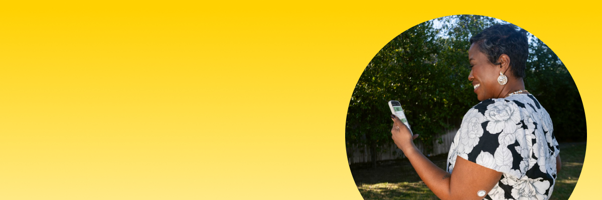 Woman smiling looking at a phone and wearing a FreeStyle Libre 3 Plus sensor