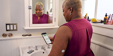 Woman doing her makeup in the mirror while wearing a FreeStyle Libre sensor