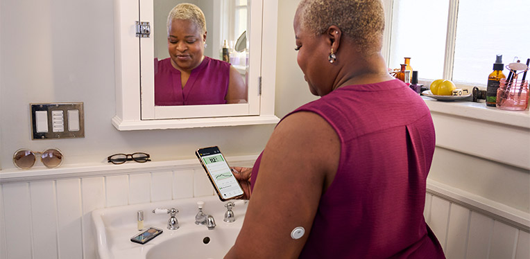 Woman doing her makeup in the mirror while wearing a FreeStyle Libre sensor