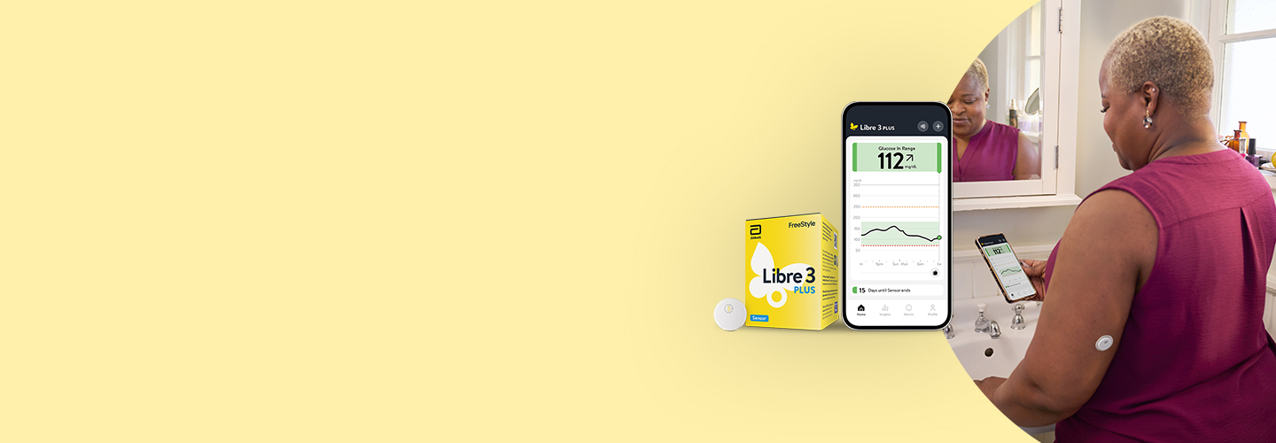 Woman standing by the bathroom mirror wearing a FreeStyle Libre 3 Plus sensor while looking at the Libre App on her phone