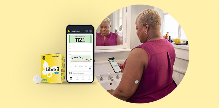 Woman standing by the bathroom mirror wearing a FreeStyle Libre 3 Plus sensor while looking at the Libre App on her phone