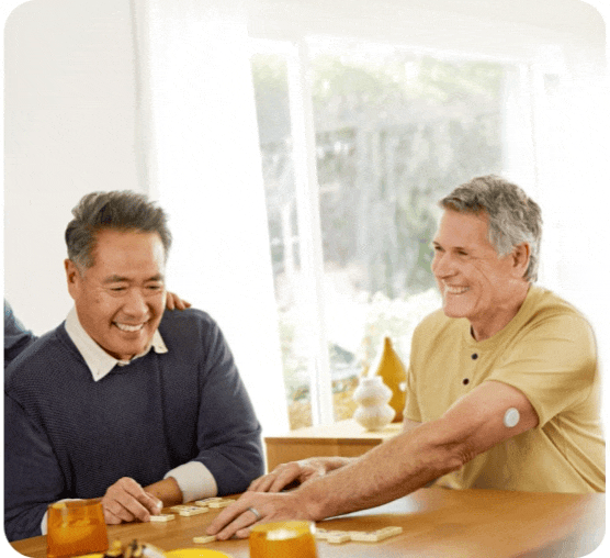 Two older men laughing while playing dominos while one man is wearing a CGM sensor