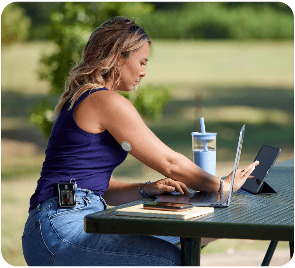 Woman working on a tablet and laptop outside while wearing a FreeStyle Libre 2 Plus sensor and Tandem t:slim X2 insulin pump