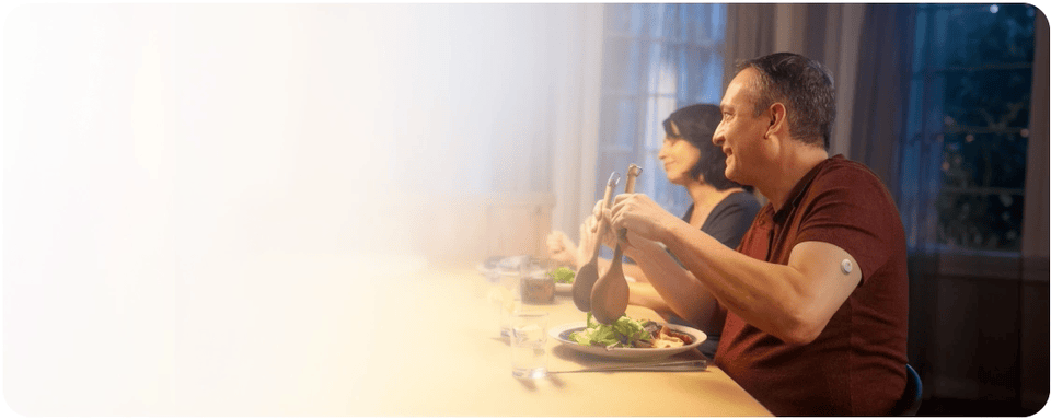 Man wearing a FreeStyle Libre CGM sensor serving salad and laughing at the dinner table