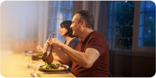 Man wearing a FreeStyle Libre CGM sensor serving salad and laughing at the dinner table