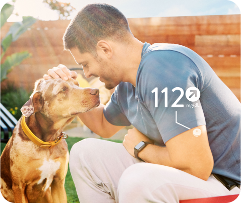 Smiling man wearing a FreeStyle Libre CGM sensor while petting a dog