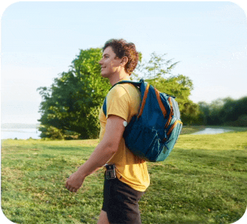 Man wearing a backpack and walking in a field while wearing a FreeStyle Libre 2 plus sensor