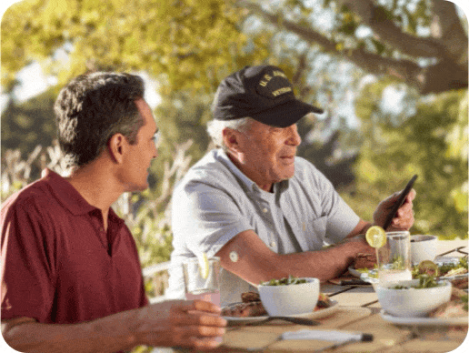 Army veteran checks his blood glucose while sitting at a picnic table while a younger man looks on