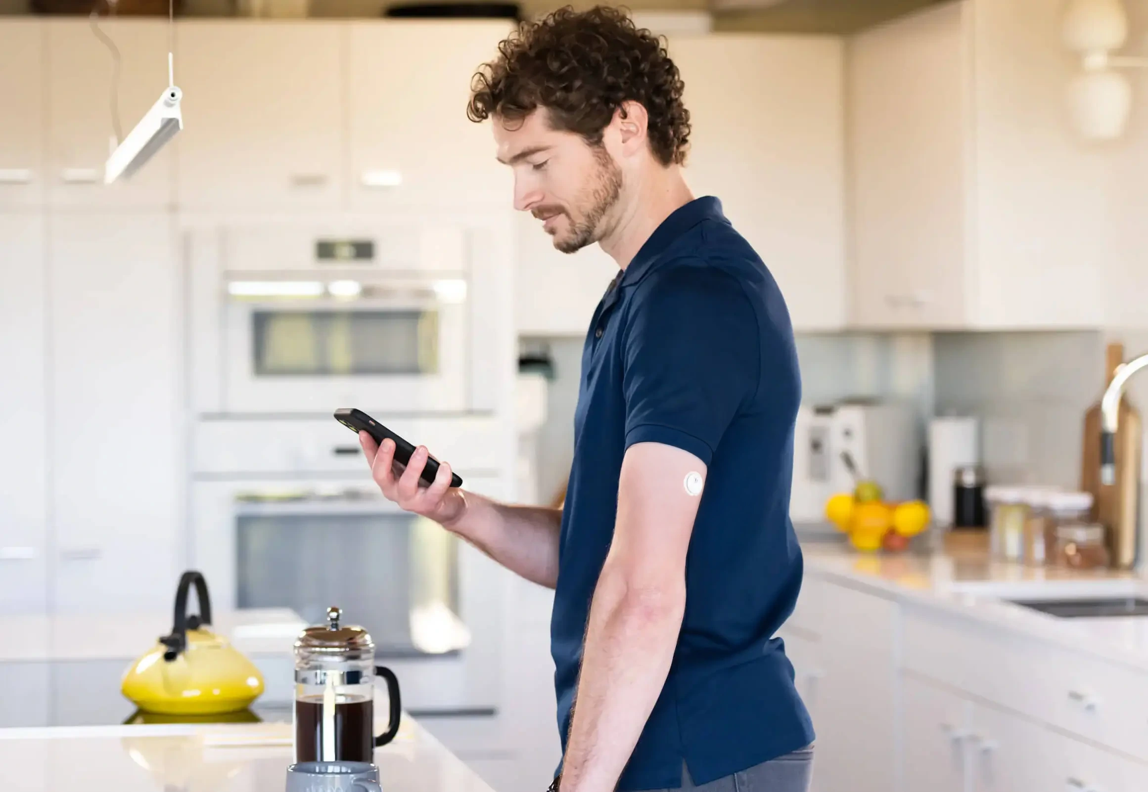 Mann mit FreeStyle Libre 3 Sensor am Arm steht in der Küche und schaut auf sein Handy