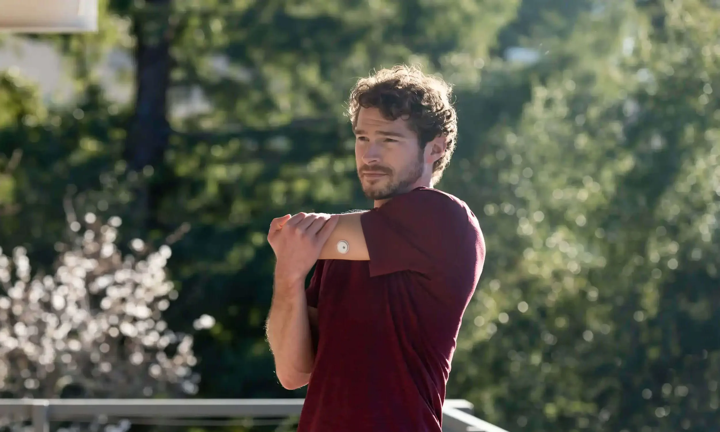 Mann mit FreeStyle Libre 3 Sensor am Arm steht in der Natur beim Stretching