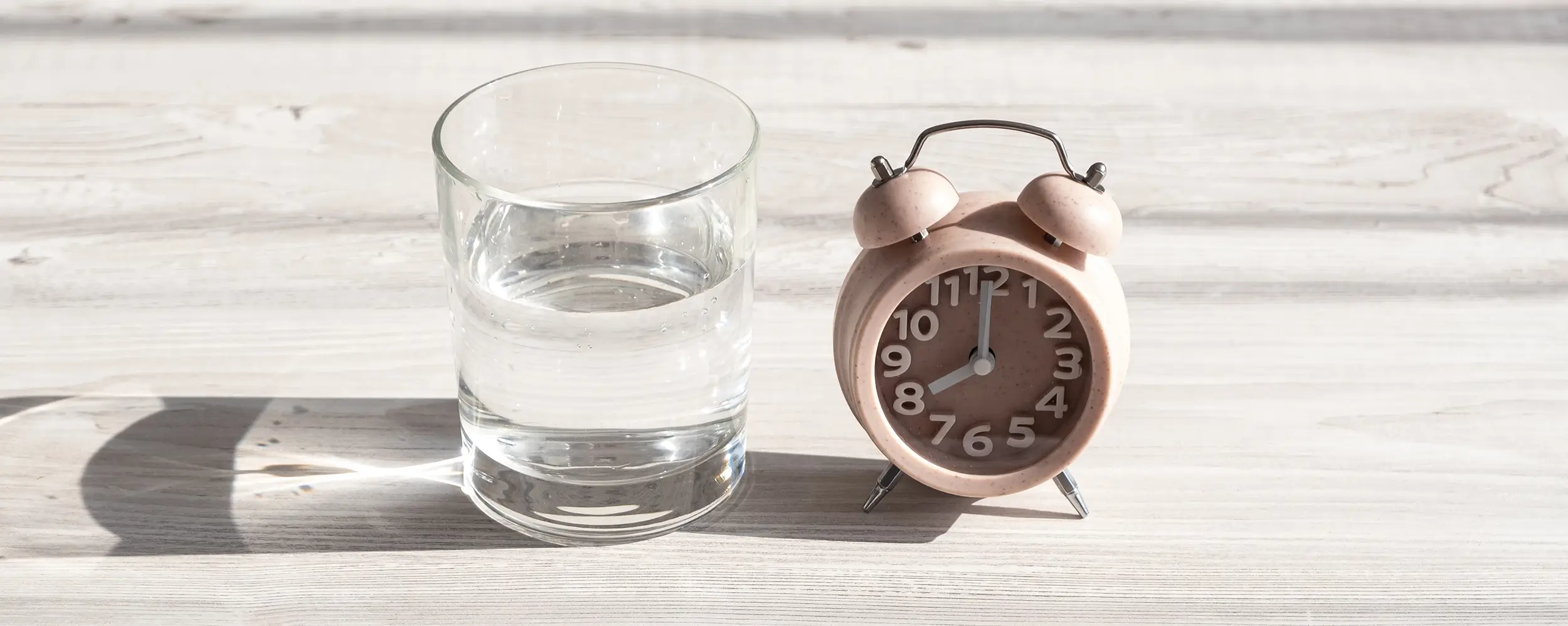 Glas Wasser und Wecker auf Nachttisch als Symbol für gesunden Schlaf – Tipps für besseren Schlaf bei Diabetes und zur Senkung des Blutzuckerspiegels.