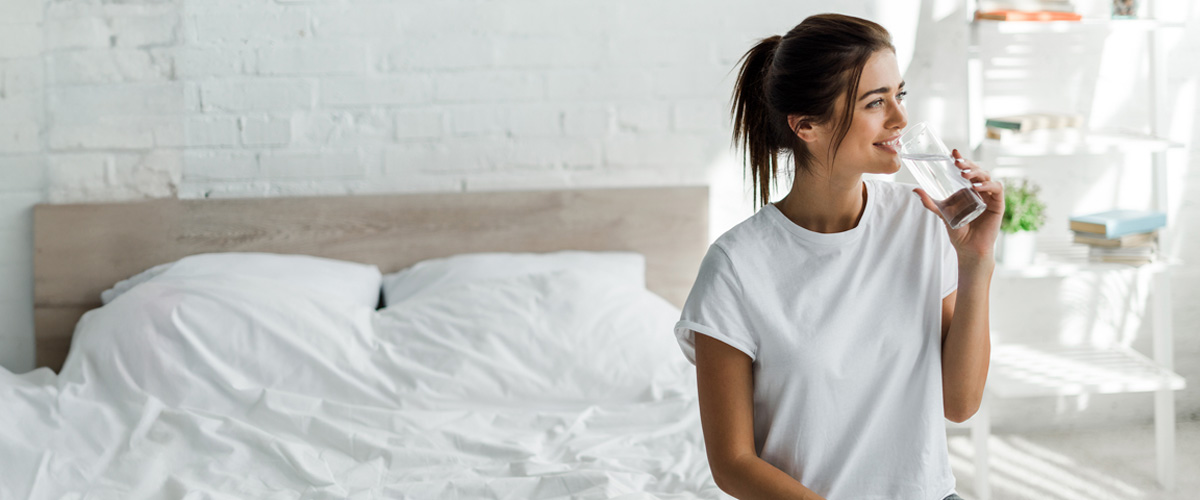 Mujer sentada en la cama bebiendo agua