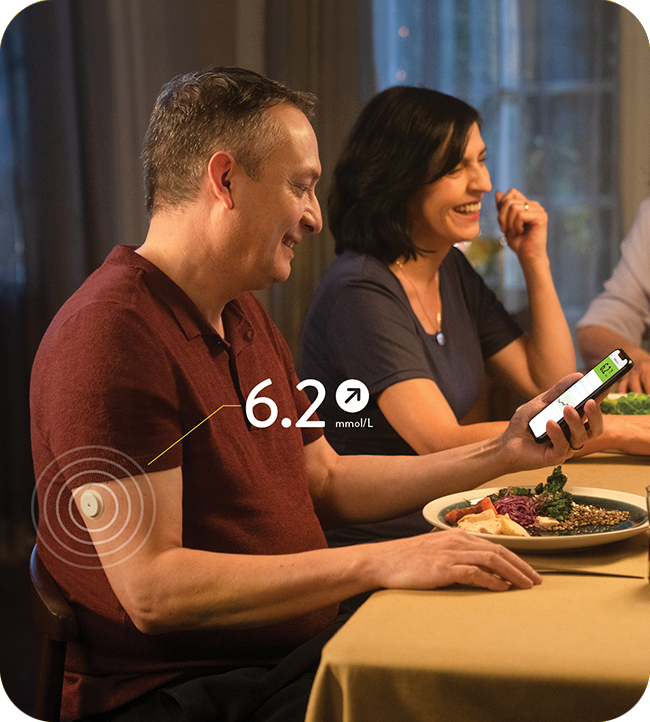 A man at dinner checking his glucose levels on his phone using the FreeStyle LibreLink app