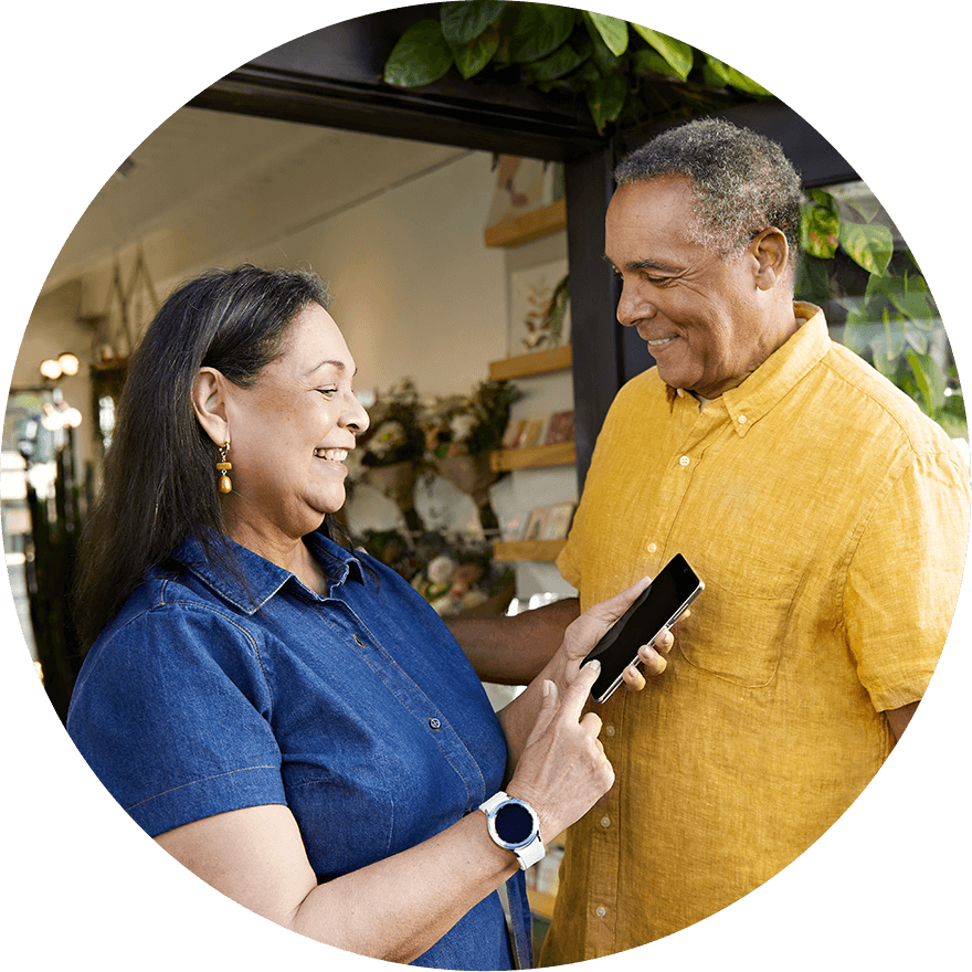 A FreeStyle Libre2  System user smiling using her phone standing with her partner, a visibile sensor can be seen on her arm.