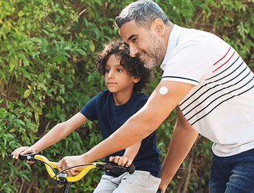 A father wearing a glucose sensor showing his son how to ride a bike.