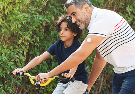 A father wearing a glucose sensor showing his son how to ride a bike.