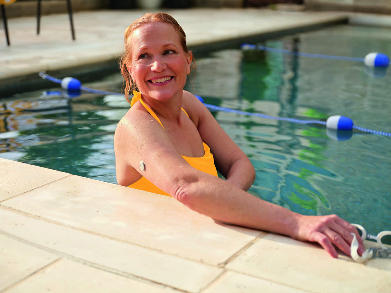 Femme souriante dans une piscine avec un capteur sur le haut du bras.