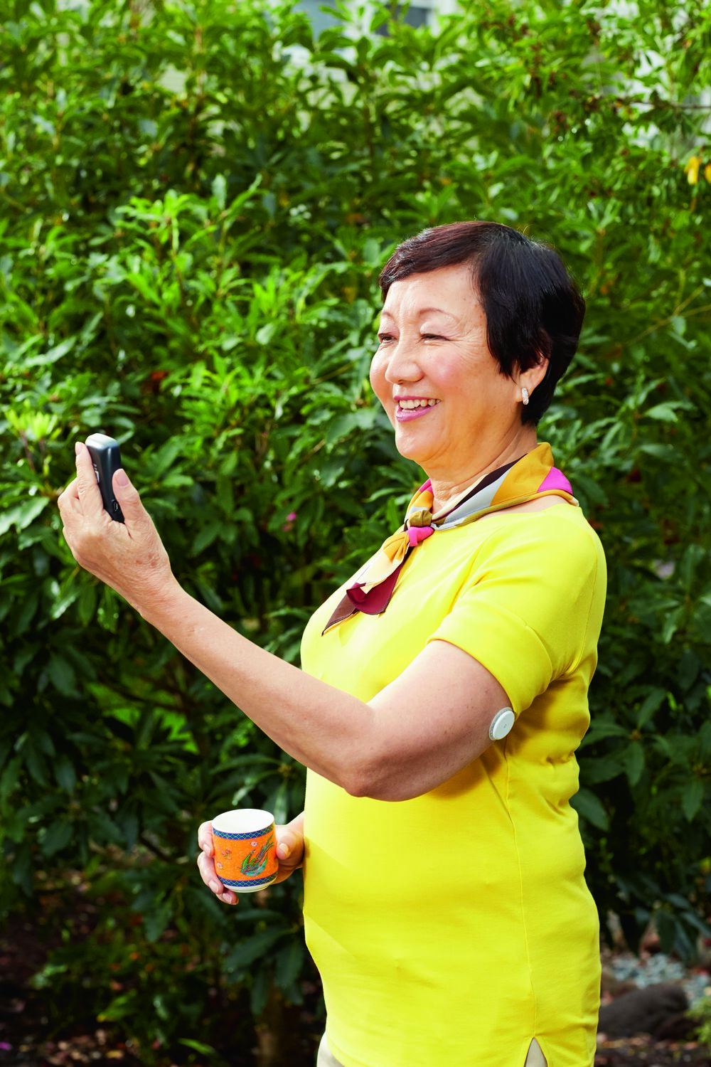 Une femme souriante avec un capteur sur le haut du bras, tenant une tasse et consultant son lecteur.