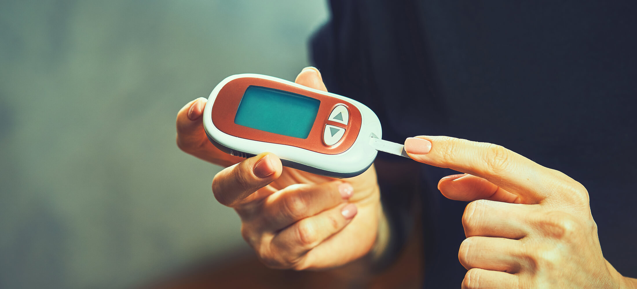 A person adds blood from a pinprick on their finger to their Blood Glucose Monitor.