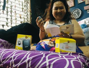 A woman sits on her bed and reads the instruction manual to her new Freestyle Libre system.