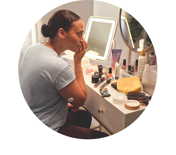 a woman applying her makeup and a FreeStyle Libre sensor is visible on her arm