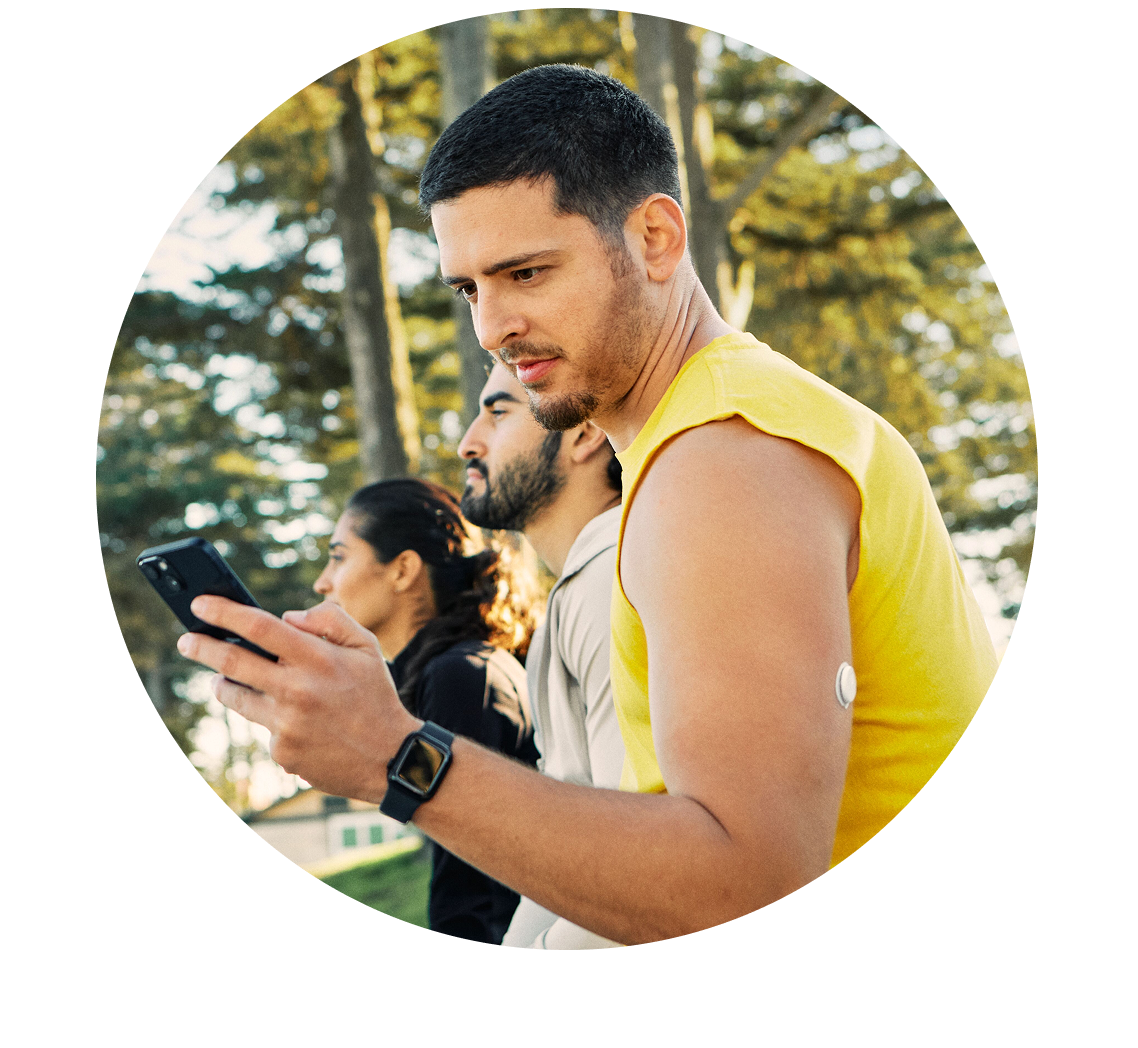Man in athletic wear sat outdoors, looking at his mobile phone. A FreeStyle Libre 2 Plus sensor is visible on his upper arm