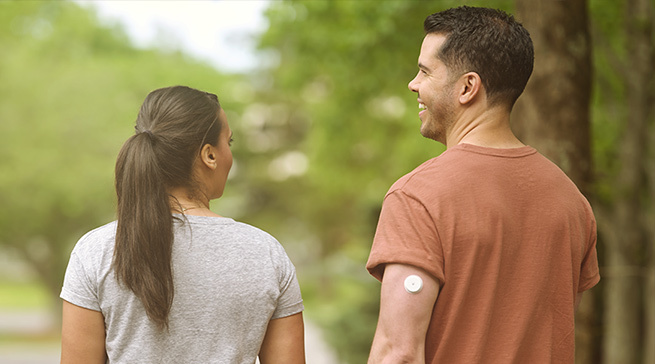 FreeStyle Libre user with Libre 2 Plus sensor visible on the back of his upper arm walking with a friend