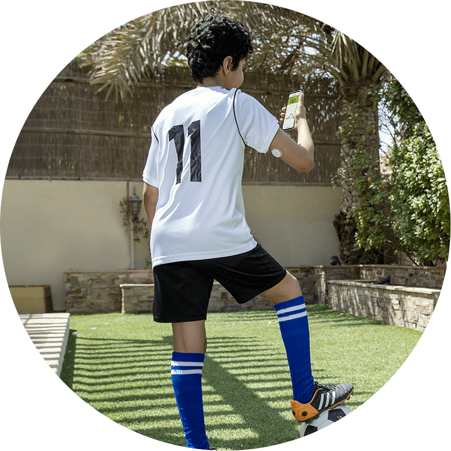 Child in football gear with sensor on his upper arm, checking his phone