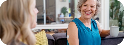 Women with coffee smiling while the FreeStyle Libre sensor is visibile on the back of her arm.