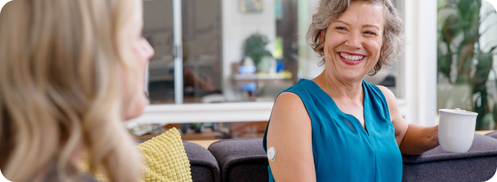 Women with coffee smiling while the FreeStyle Libre sensor is visibile on the back of her arm.
